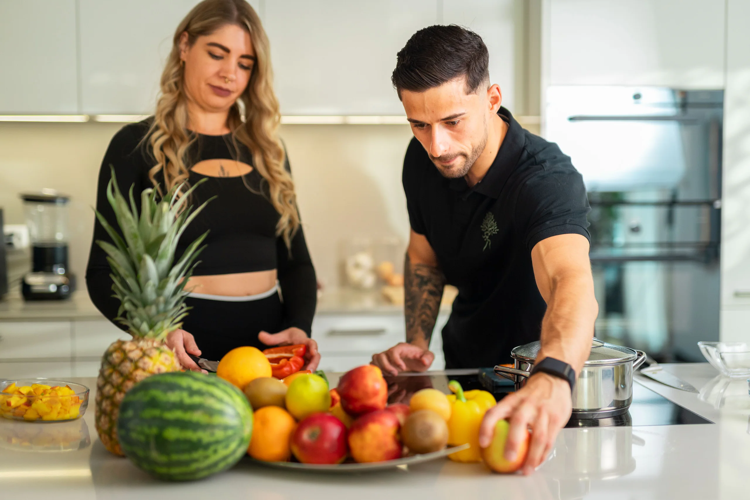 Ernährungscoach und Kundin an der Küchentheke mit Ananas, Wassermelone und frischem Obst