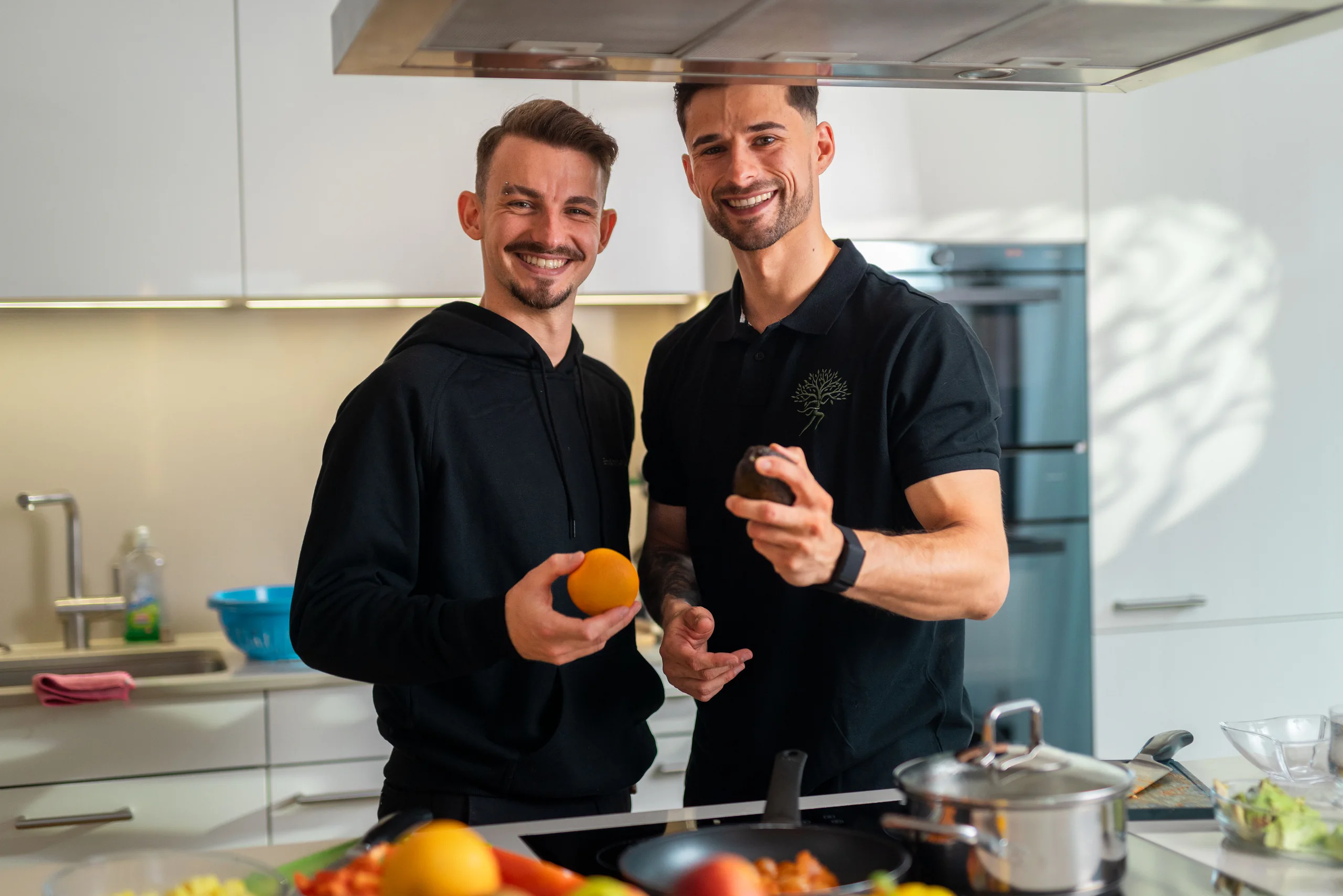 Zwei Coaches lachen in der Küche mit Orangen in der Hand