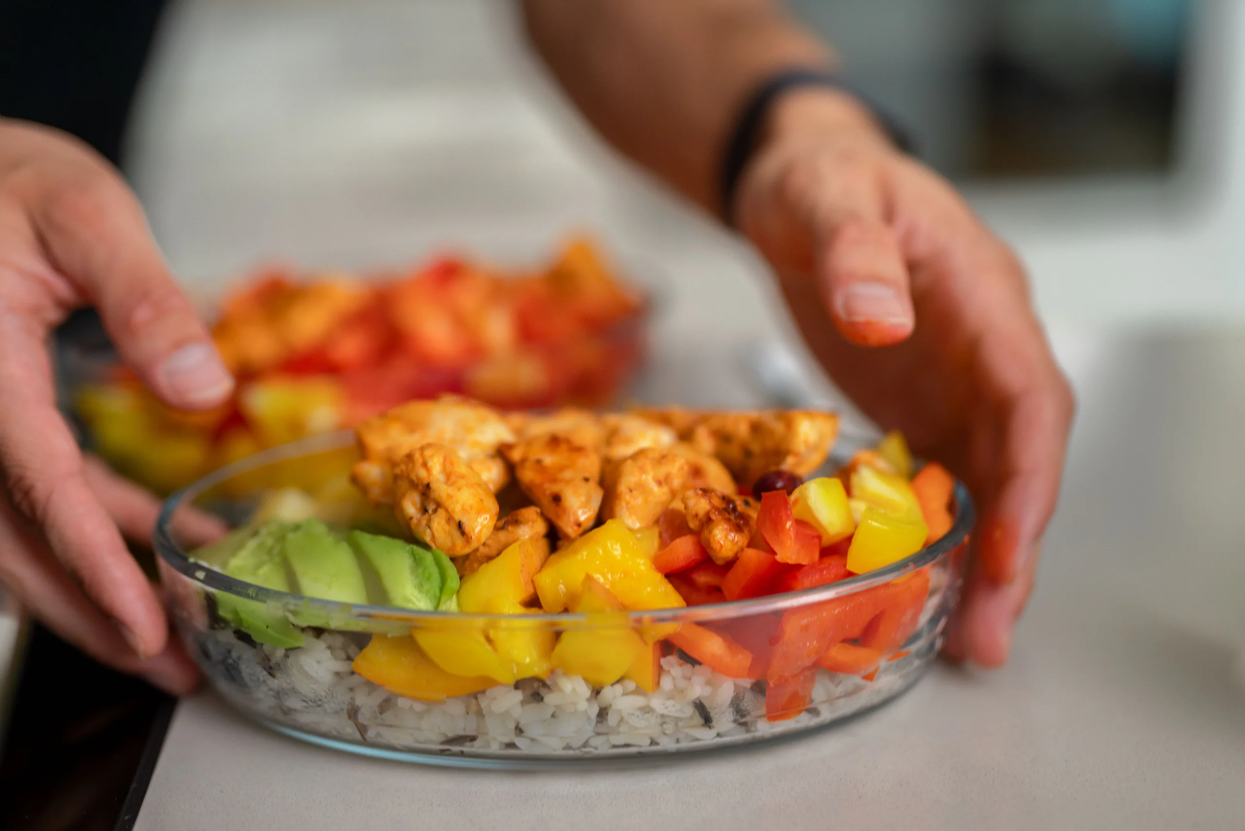 Hände richten eine Bowl mit Poulet, Avocado und Peperoni an