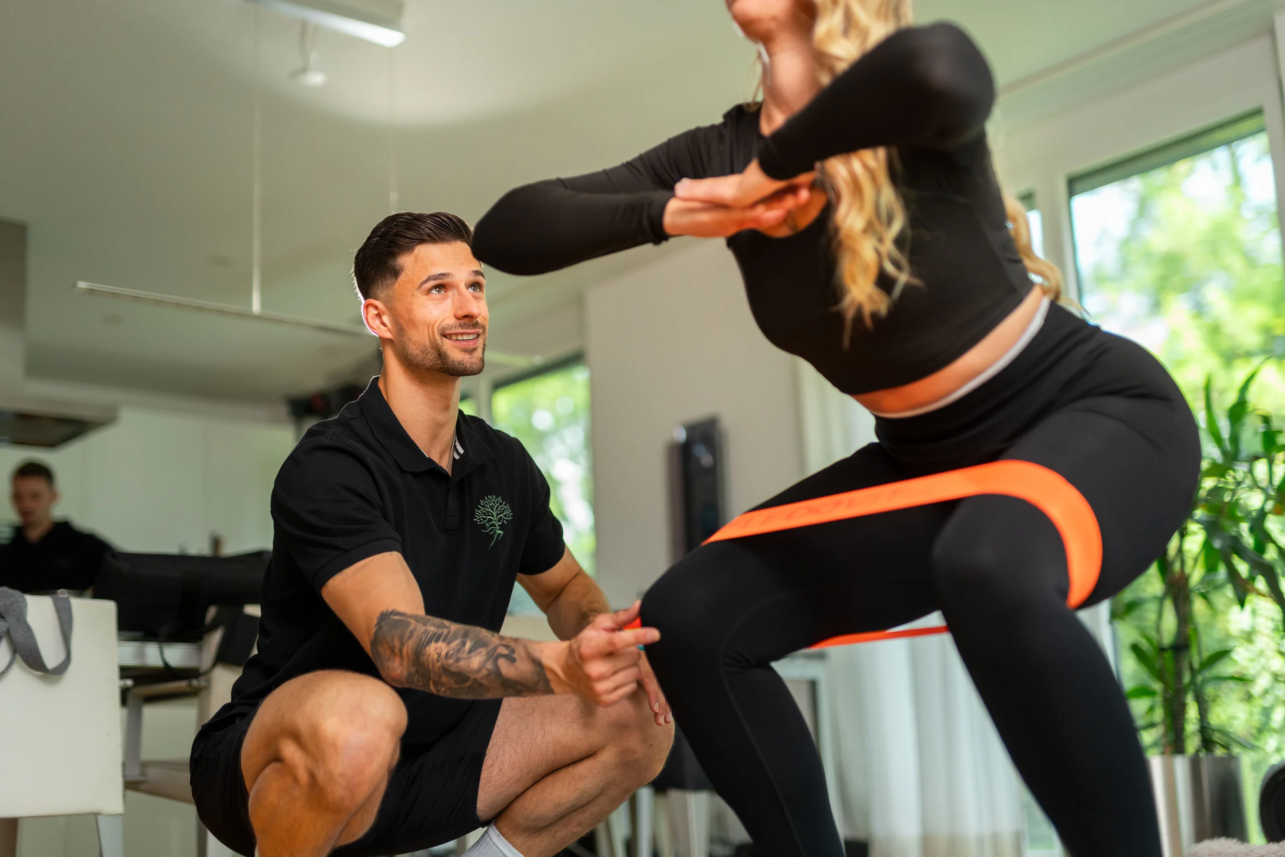 Kundin macht Kniebeugen mit Widerstandsband, der Coach korrigiert die Haltung
