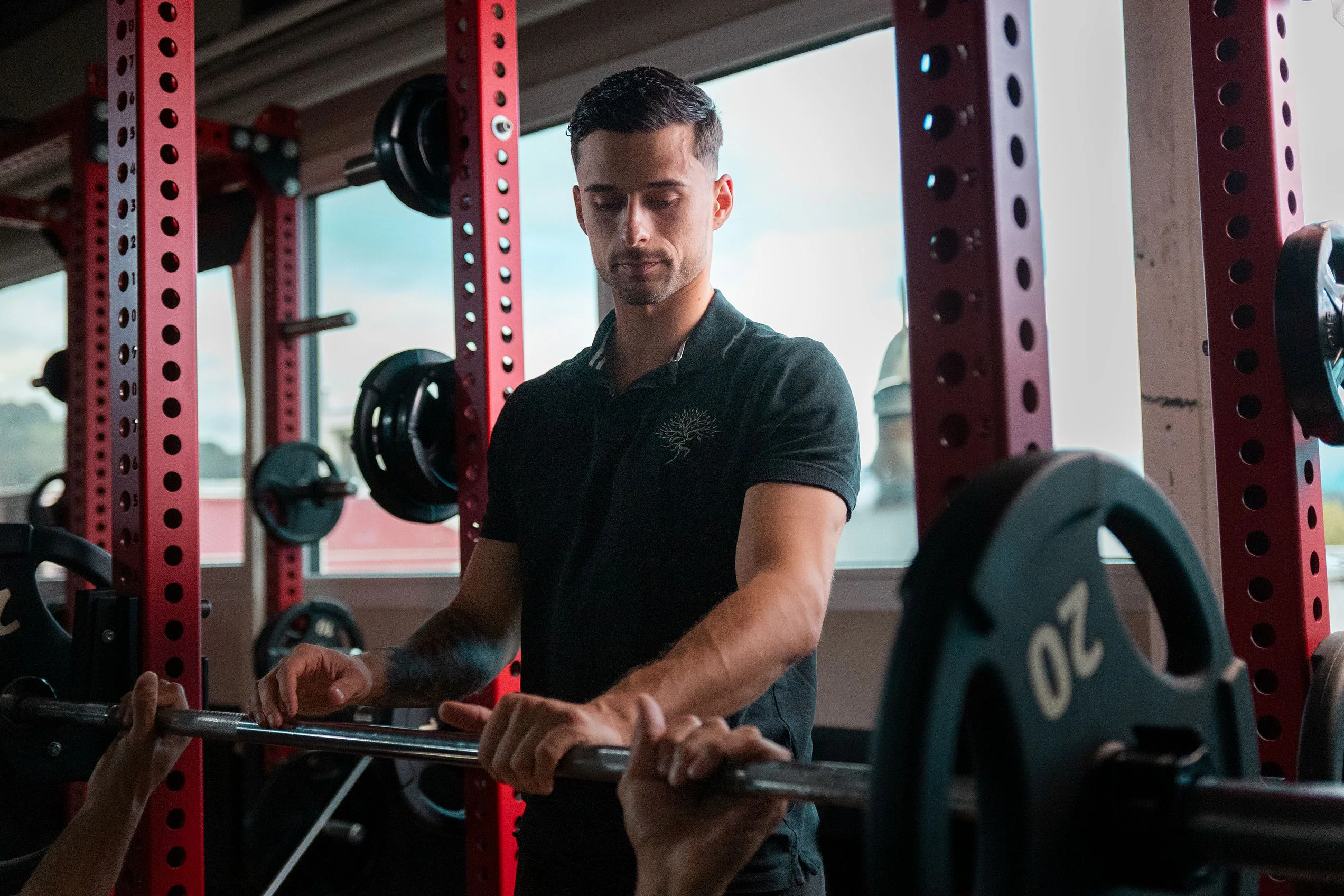 Coach mit Langhantel am Rack im Fitnessstudio