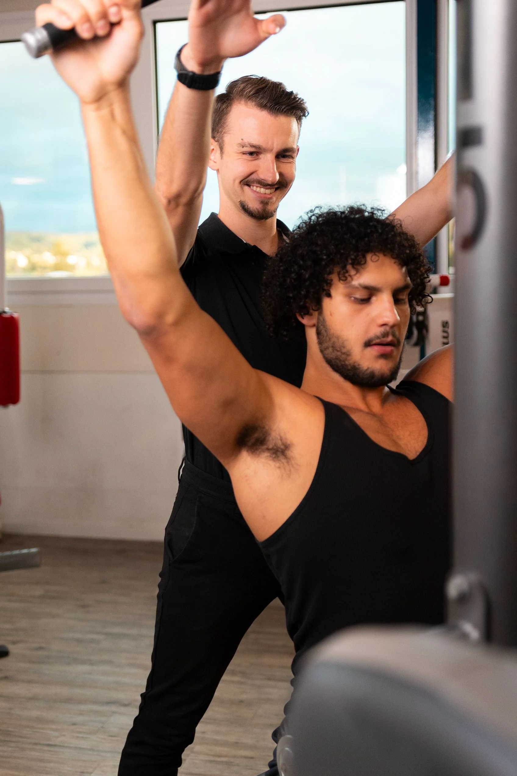 Coach hilft einem Kunden bei einer Übung mit erhobenen Armen im Fitnessstudio