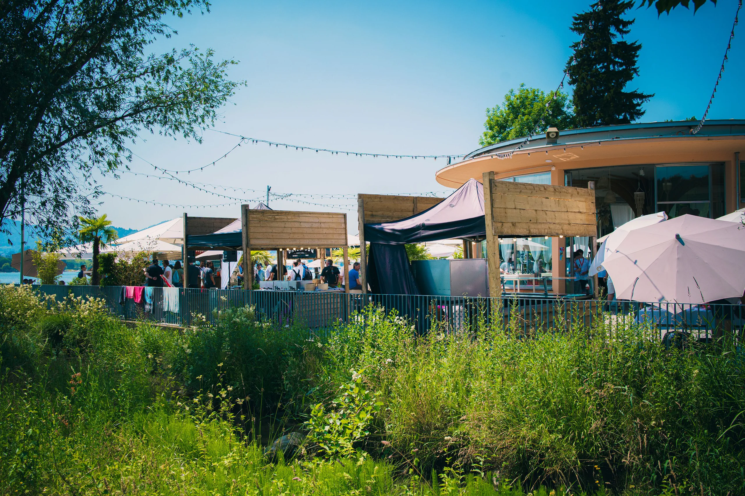 Festgelände am See mit Pavillons und Sonnenschirmen