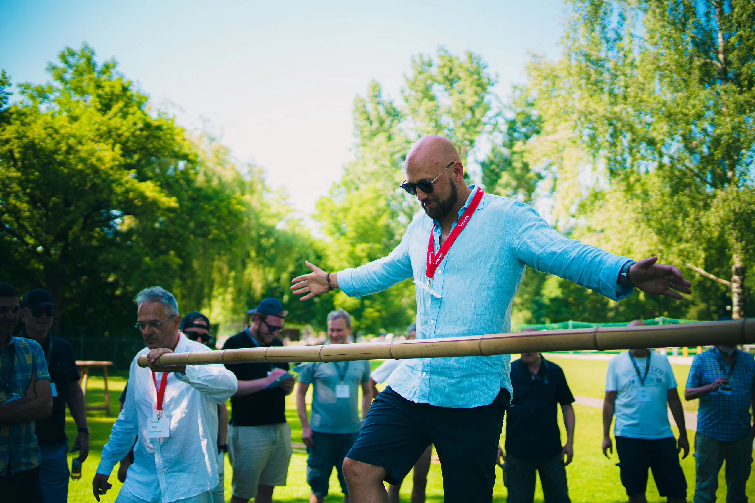 Gast balanciert auf einem Bambusstamm, Kolleginnen und Kollegen schauen zu